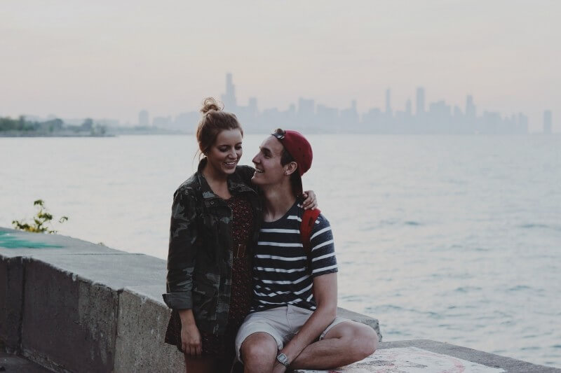 young-couple-sitting-on-ledge-embracing-and-smiling
